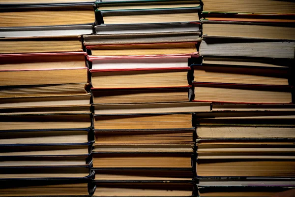 Shelves with old books. Stacks of textbooks with red, blue, green covers and paper sheets with shadow in a dark library. Stacked retro books in a bookstore