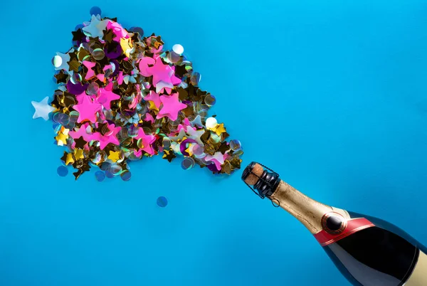 Bottle of champagne with splash of sparkling iridescent confetti on blue screen background. Mock up from pink, gold and purple glitter stars and circles with workspace. Sequins, tinsel for valentines