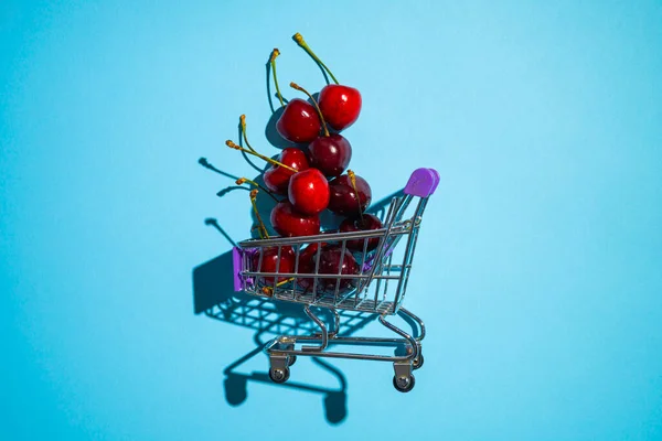 Ripe Red Sweet Cherries Small Shopping Cart Blue Background Juicy — Zdjęcie stockowe