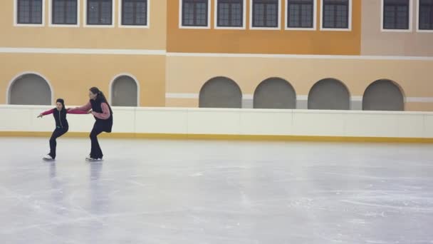 スケートの女の子を説明するプロのフィギュアスケートコーチは 彼女の手を取り 右の位置を示す 移動する方法 明るい氷のアリーナで研修生の近くに移動若いフィギュアスケートトレーナー ゆっくり — ストック動画