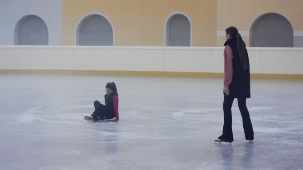 若い女性フィギュアスケートコーチは 氷のアリーナで氷から立ち上がるために落ちた女の子を助ける コーチは動揺した少女を落ち着かせる リンク 失敗でフィギュアスケートのトレーニング スローモーション — ストック動画