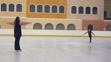 Arkaya bakan bir bayan buz pateni koçu öğrencisine bakıyor ve tavsiye veriyor. Küçük kız buz pateni yaparken parlak bir buz arenasında kayıyor. Işıl ışıl yanan buz pateni pistinde antrenman