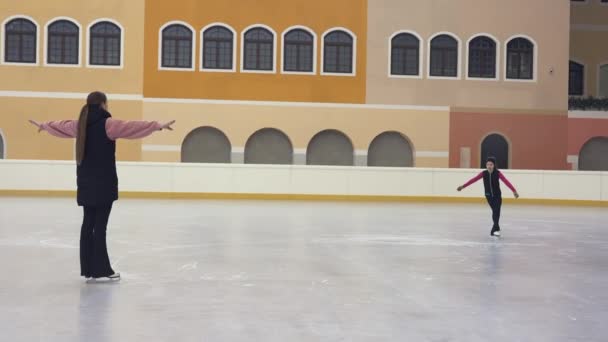 一个女子花样滑冰教练回头看她的学生并给出建议 小女孩在明亮的冰场上滑行 练习花样滑冰技巧 有关明亮的冰场的培训 — 图库视频影像