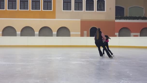 スケートの女の子を説明するプロのフィギュアスケートコーチは 彼女の手を取り 右の位置ジャンプを示す 移動する方法 若いですフィギュアスケートトレーナー移動近く研修生オン明るいです氷のアリーナ — ストック動画