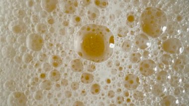 Top view of golden liquid with white foam and bursting bubbles. Macro shot of an amber foamy beer, cider or lagar. Carbonated soda or yellow oil. Beautiful textured beer background for advertising for