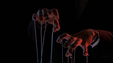 Kukla kuklaları elle manipüle etmek. Siyah yalıtılmış sırt çantasının üzerinde kukla ipleri olan erkek eller. Yöneticileri kontrol eden siyah takım elbiseli patron. İş gücü. Konsept