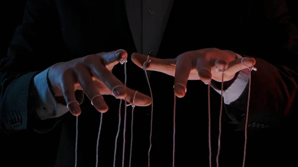Man hands with strings on fingers. Hands close up pulling strings, manipulating, controlling. Man in business suit manipulates puppet. Puppeteer, marionettist. Boss controlling his managers