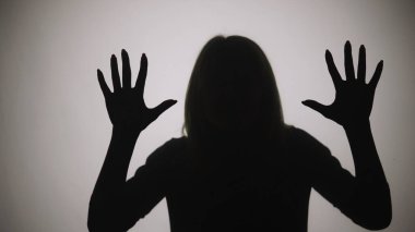 Avuçlarıyla cama dokunan ve kameraya bakan bir kadının siyah silüeti. Beyaz mat ışığı olan bir pencerenin arka planına dayanan bir kadın çizgisi. Model stüdyoda birlikte poz verir