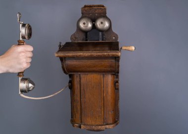El ele tutuşmak, ahşap kahverengi antika telefon cihazından çıkarılmış. Gri stüdyo arka planında sinyal vermek için iki metal yarım küresi olan eski püskü bir telefon. Eski ahizeli eski telefon