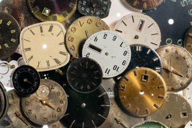 Yıpranmış saatlerin üst görüntüsü. Elleri ve numaraları olan yaşlanmış yuvarlak saat yüzleri. Beyaz, siyah ve metal, kırık ve parçalanmış saat göstergeleri. Atölyede antika saat, tamir