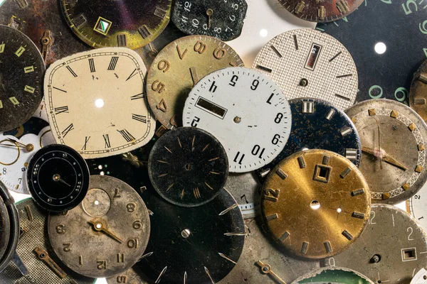 Yıpranmış saatlerin üst görüntüsü. Elleri ve numaraları olan yaşlanmış yuvarlak saat yüzleri. Beyaz, siyah ve metal, kırık ve parçalanmış saat göstergeleri. Atölyede antika saat, tamir