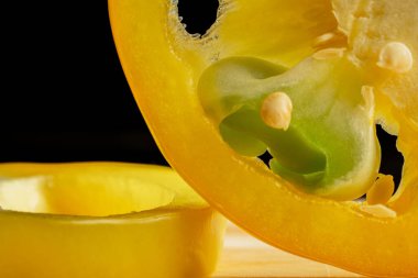 Dilimlenmiş taze çiğ sarı dolma biber halkaları ahşap tahtada, izole edilmiş siyah stüdyo arka planında. Çekirdekli tatlı biber dilimleri ve makro fırında sulu posa. Olgun sebzelerin arka planı