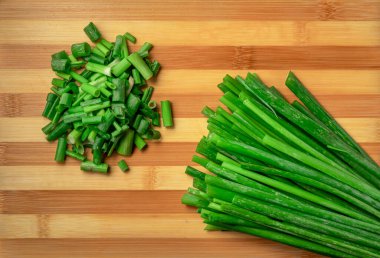Çizgili ahşap mutfak tahtasının üzerinde taze taze soğan parçaları ve sapları var. Sulu yeşil soğan ya da soğan dilimleri ve sapları. Yeşillik, taze sağlıklı salata pişirmek için baharat. Kapat.