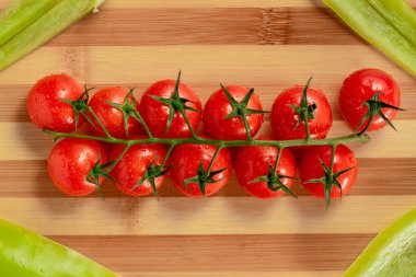 Bir demet olgun kırmızı kiraz domatesleri ve çizgili tahta üzerinde doğranmış yeşil tatlı biber parçaları. Domates ve nemden sırılsıklam olmuş tatlı biber manzarası. Mutfakta taze sebzeler