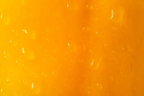 Macro shot of yellow peel of a sweet pepper or tomato with water drops. The texture of the yellow wet surface of a vegetable covered with drops of moisture or dew. Yellow background for screensaver or