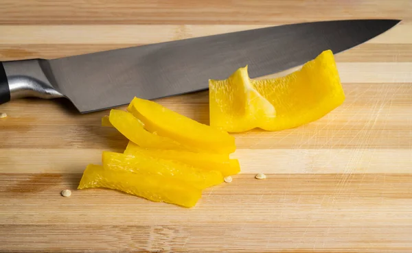 Sliced pieces of yellow sweet pepper and a metal sharp knife on a wooden board. Juicy pulp of yellow bell pepper and seeds on a cutting board. Background of ripe vegetables for restaurant. Fresh