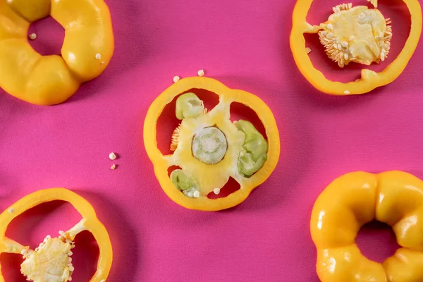 Sliced rings of yellow sweet pepper on a pink background. Top view of sweet pepper pieces with juicy pulp and seeds. Fresh ripe sliced vegetables close up. Fresh raw ingredients for salad. Background