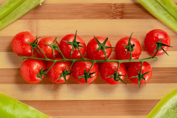 Bir demet olgun kırmızı kiraz domatesleri ve çizgili tahta üzerinde doğranmış yeşil tatlı biber parçaları. Domates ve nemden sırılsıklam olmuş tatlı biber manzarası. Mutfakta taze sebzeler