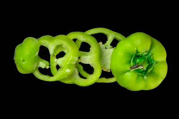 Green sweet pepper cut into rings on a black wooden table or kitchen board surface. Top view of round pieces of sliced bell peppers with seeds and juicy pulp. Rows of sliced vegetables close up