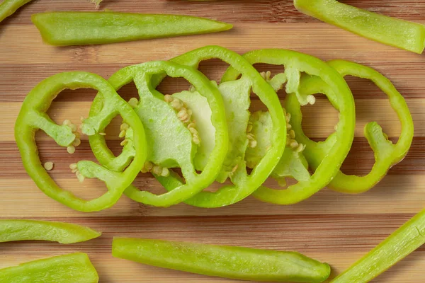 Green sweet pepper sliced into rings on a striped wooden board. Top view of round slices and pieces of yellow bell peppers with seeds and juicy pulp. Sliced wet vegetables on wooden table close up