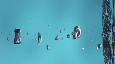 Suyun sakin yüzeyinde yükselen ve patlayan parlak hava kabarcıkları. Kaplara dökülen temiz mavi sıvının tazeliği. Şeffaf mavi su ve ışık parlaması. Sıvının çekimini kapat