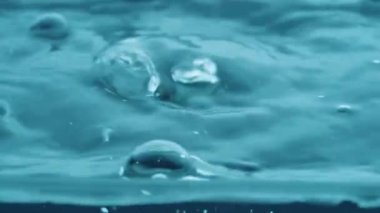 Kabaran su yüzeyinde hava kabarcıkları yükseliyor. Mavi şeffaf sıvı titreşimler yüzeyde sıçramalar ve dalgalanmalar yaratır. Kaynar su, kaynayan su. Şeffaf mavi su. Yakın plan.