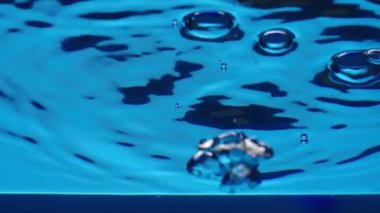 Su sütununda yükselen parlak hava kabarcıklarının alt görüntüsü yüzeyde dalgalar ve dalgalar oluşturur. Kaplara dökülen berrak mavi sıvının tazeliği. Şeffaf mavi su ve ışık parlaması. Kapat