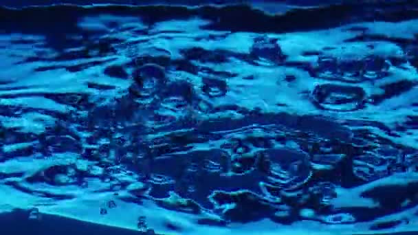在水柱中升起闪亮的气泡 在水面上形成波浪和飞溅的底部视图 清澈的蓝色液体倒入容器中 浅光的透明蓝水 — 图库视频影像