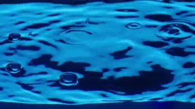 Su sütununda yükselen parlak hava kabarcıklarının alt görüntüsü yüzeyde dalgalar ve dalgalar oluşturur. Kaplara dökülen berrak mavi sıvının tazeliği. Şeffaf mavi su ve ışık parlaması. Kapat