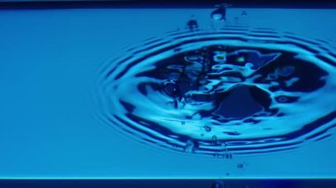 Damlalar damlayan, dalgalar ve dalgalanmalar oluşturan su yüzeyinin alt görüntüsü. Yakın plan mavi şeffaf sıvı, hava kabarcıkları ve su sıçraması. Kaplara dökülen temiz mavi sıvının tazeliği