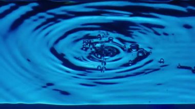 Damlalar damlayan, dalgalar ve dalgalanmalar oluşturan su yüzeyinin alt görüntüsü. Yakın plan mavi şeffaf sıvı, hava kabarcıkları ve su sıçraması. Kaplara dökülen temiz mavi sıvının tazeliği