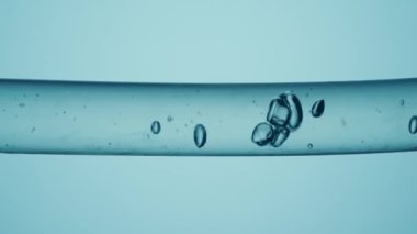 Farklı boyutlarda temiz baloncuklardan oluşan bir makro çekim. Açık mavi arka planda temiz sıvı ile cam tüp içinde akıyor. Temiz sıvı maddeli ve hareket eden baloncuklu bir kap. Kimyasal ya da biyolojik kavram
