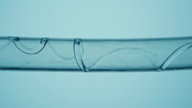 İnce bir derede akan su izole edilmiş mavi bir zeminde cam bir tüpün içindeki spiral. Temiz bir sıvı tüpü doldurup küçük hava kabarcıkları oluşturuyor. Laboratuvar araştırmaları, kimyasal deneyler.