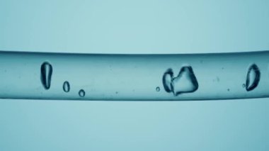 Farklı boyutlarda temiz baloncuklardan oluşan bir makro çekim. Mavi arka planda sıvı bulunan cam bir tüpte akıyor. Temiz sıvı maddeli ve hareket eden baloncuklu bir kap. Kimyasal veya biyolojik araştırma kavramı
