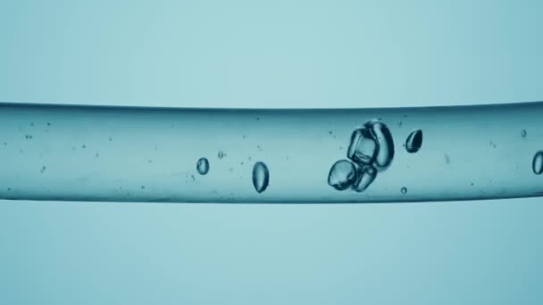 不同尺寸的透明气泡在玻璃管中流动的宏观镜头 透明液体在浅蓝色背景上流动 具有清晰液体物质和流动气泡的容器 化学或生物概念 — 图库视频影像