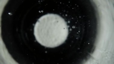 Makro yuvarlak beyaz tablet çözünür aspirin, koyu arkaplanda bir bardak suda fokurduyor. Asetilsalik asit tableti suda çözünür ve birçok tıslama kabarcığı oluşturur. Baş ağrısı
