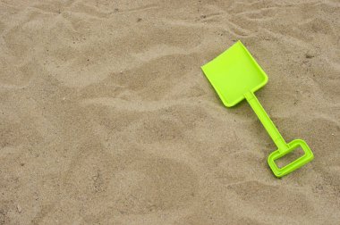 Kahverengi kumların arka planında fotokopi alanı olan parlak yeşil plastik oyuncak kürek 