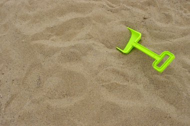 Kahverengi kumların arka planında fotokopi alanı olan parlak yeşil plastik oyuncak kürek 