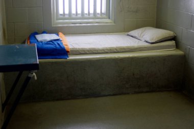 Yatak ve parmaklıklı pencereli hapishane hücresi