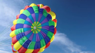 Çok renkli bir paraşüt, sirrus bulutlu mavi bir gökyüzüne karşı. Deniz kıyısında parasailing.
