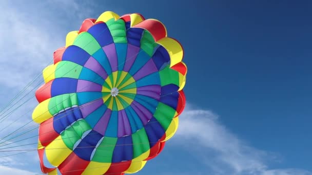 在蓝天和卷云的映衬下，一个多色的飘扬的降落伞。海岸上的跳伞. — 图库视频影像