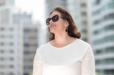 Şehir ortamında binaların arasında şık kıyafetler ve güneş gözlüğü takan klasik beyaz kadın..