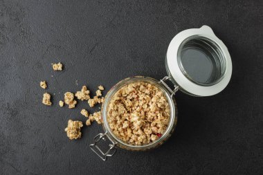 Kavanozda granola, karanlık masada. Siyah arka planda sağlıklı yiyecekler. Üst görünüm.