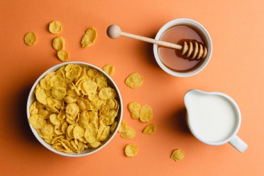 Sütlü mısır gevreği ve turuncu arka planda bal. Sağlıklı kahvaltı manzarası.