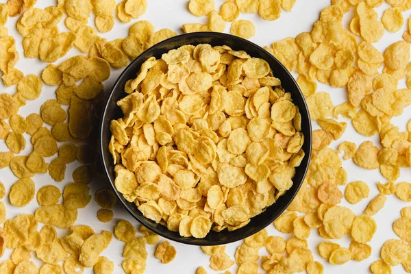 Corn flakes in dark bowl on white background. Top view of healthy breakfast.