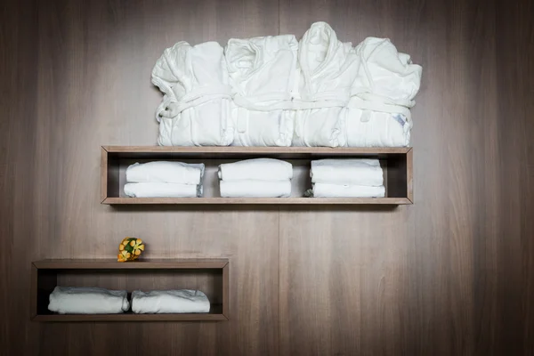 Vita badrockar och handdukar häftade på brunt trä hylla med blommor — Stockfoto