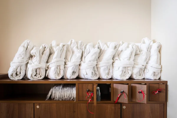 Arranged white bathrobes on cupboard with wooden lockable boxes — Stock Photo, Image