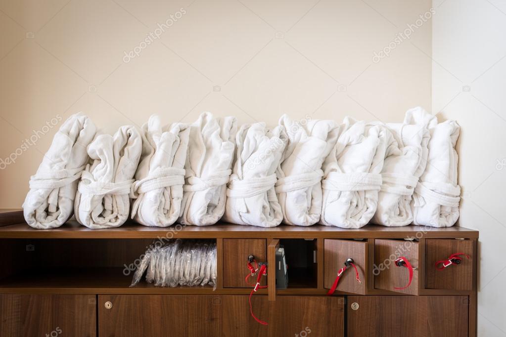 Arranged white bathrobes on cupboard with wooden lockable boxes