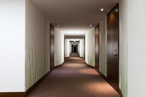 Lång hotellkorridor med dörrar och grön gräsmatta tapet — Stockfoto