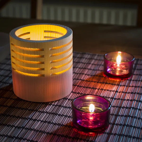 Tea candles in wood and glass standing on reed mat — Stock Photo, Image